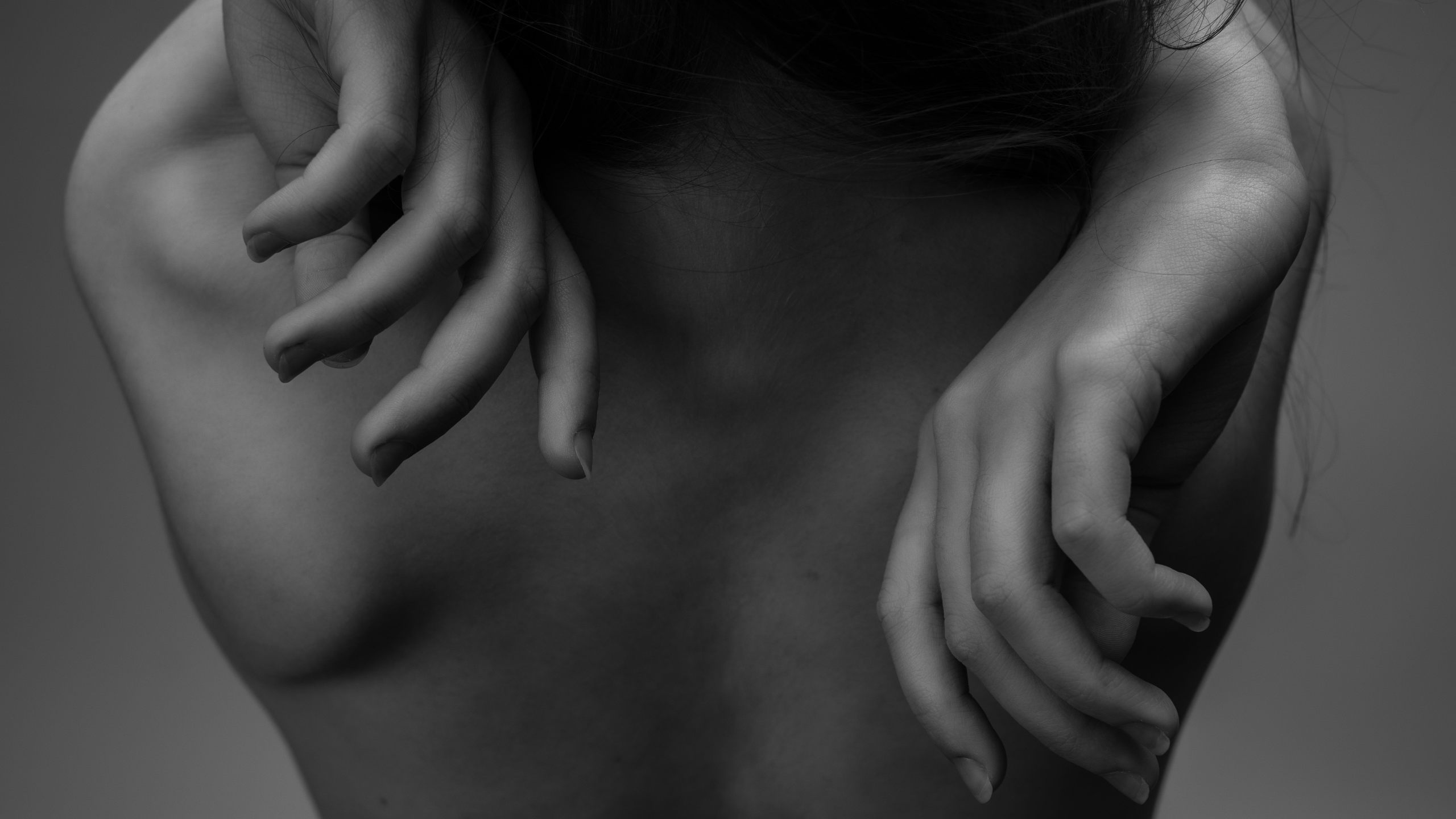 The baked back of a woman with both hands resting on her shoulders