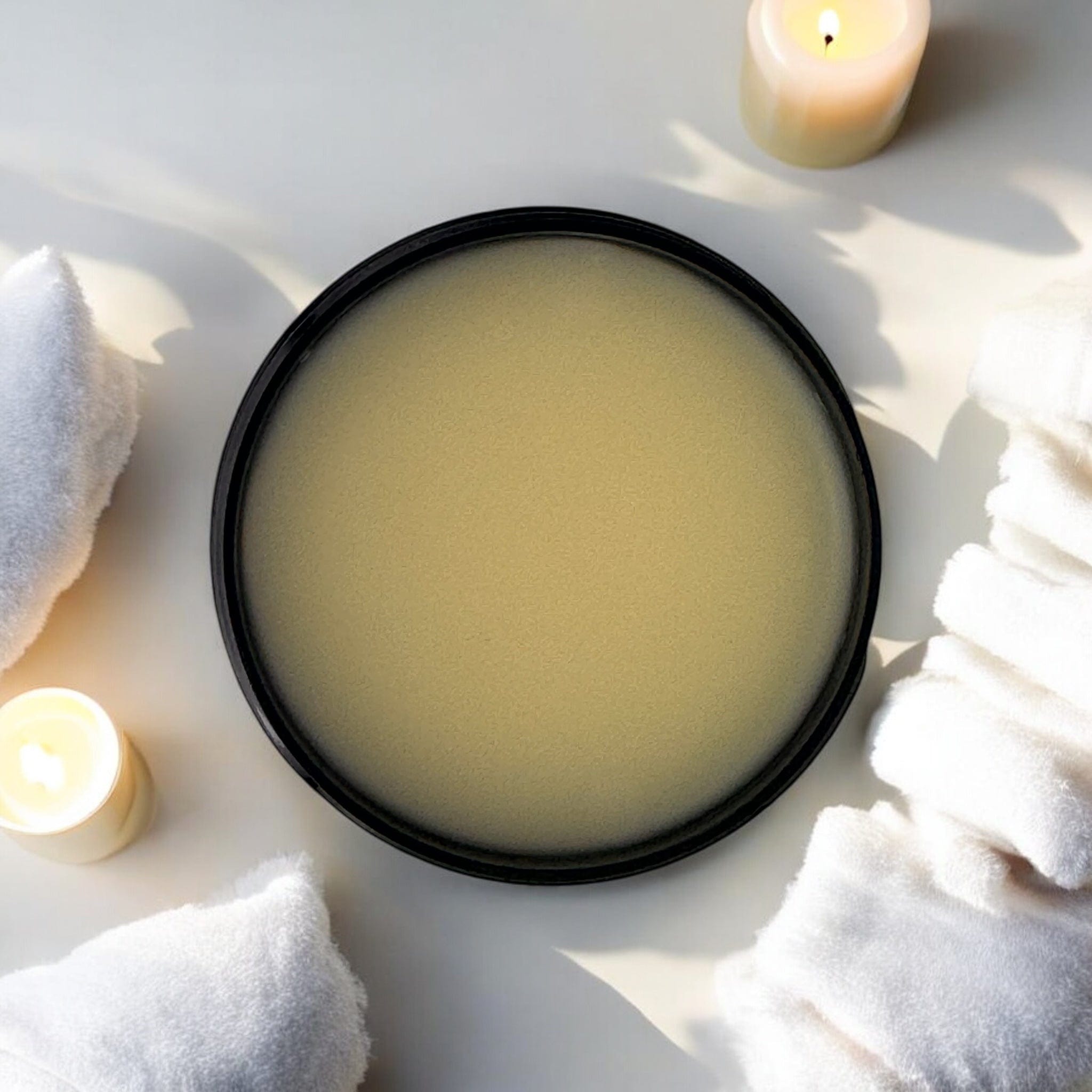 Open container of pale yellow muscle balm with natural skincare and botanical ingredients, surrounded by white towels and. - Muscle Balm - PUREMESS SKINCARE